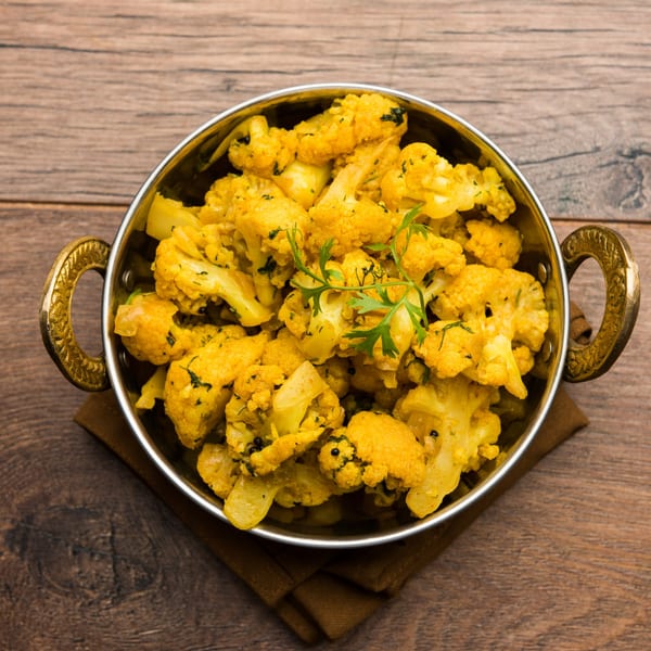 Indian Gobi Aloo, a cauliflower and potato curry, in a brass bowl on a wooden table.