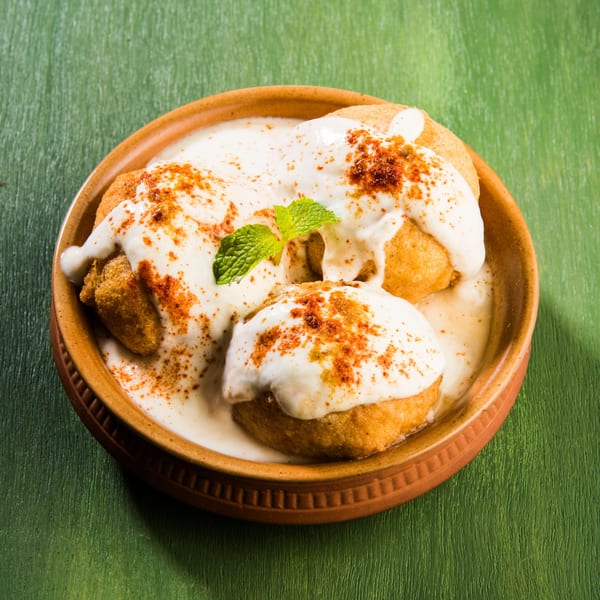 Dahi Vada, a popular Indian snack, in a brown bowl with white yogurt, spices, and mint.