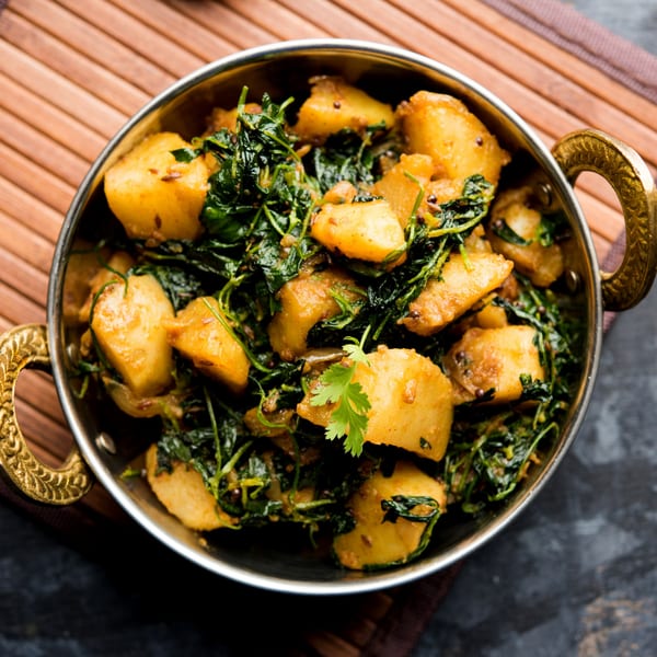 Indian Aloo Methi, a dish of potatoes and fenugreek leaves, served in a brass bowl.