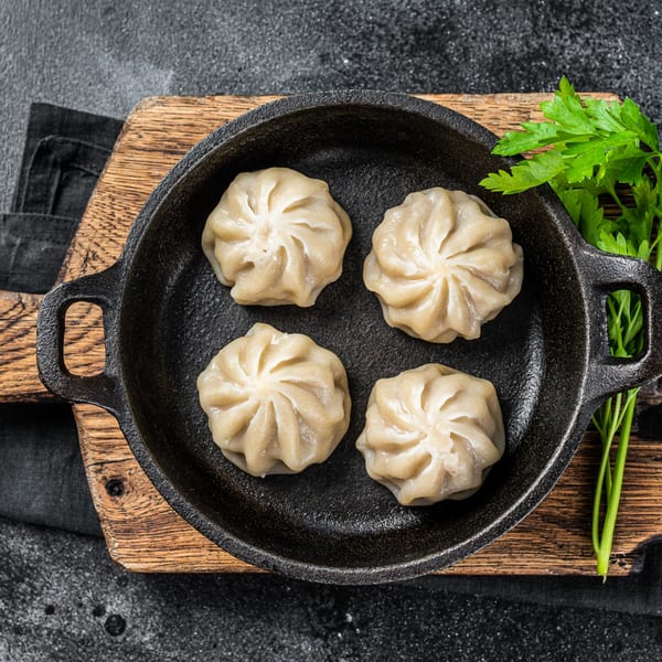 Four steamed momos, a type of Indian dumpling, in a black cast iron pan with parsley.